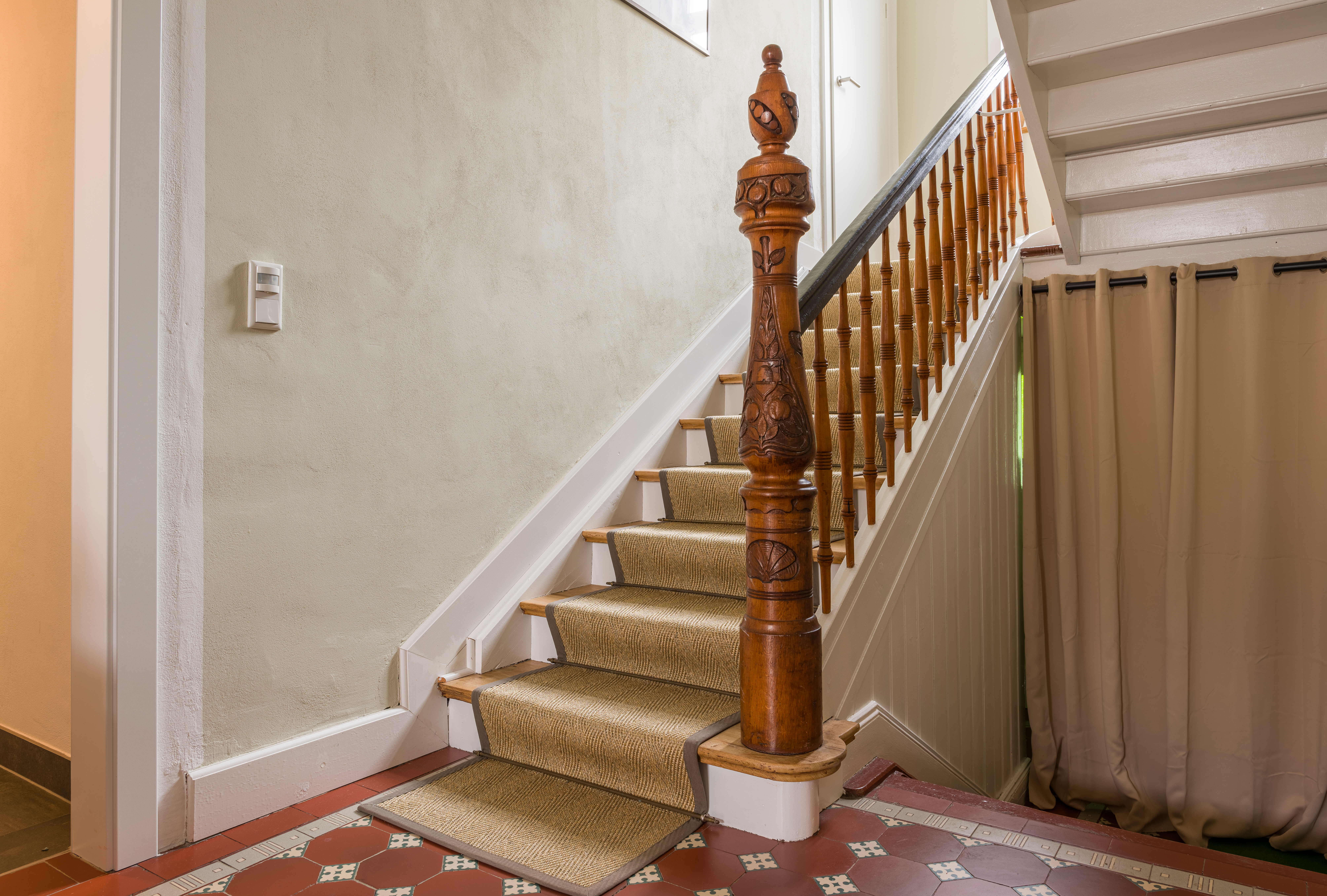 Blick in das Treppenhaus mit den originalen Fliesen und dem kunstvoll geschnitzten Geländerpfosten