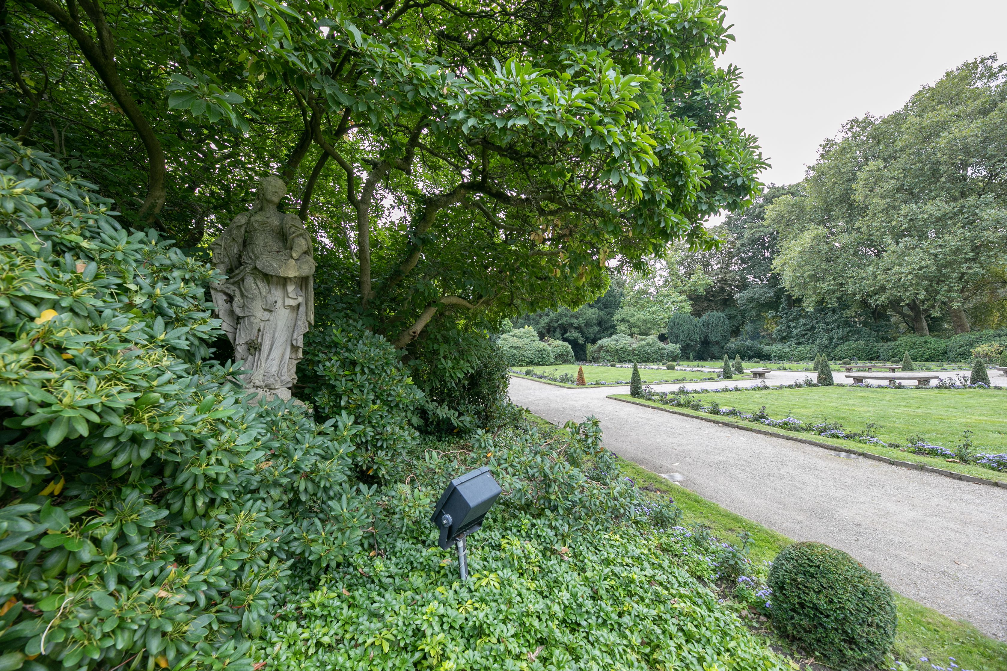 Sandsteinplastiken inmitten dunkellaubiger Rhododendren