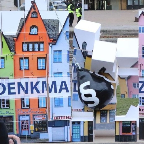 Abrissbirne prallt gegen ein Haus aus Papier auf dem "Denkmalschutz" steht