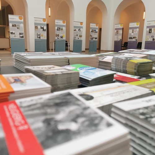 Flyerstapel mit Ausstellung im Hintergrund