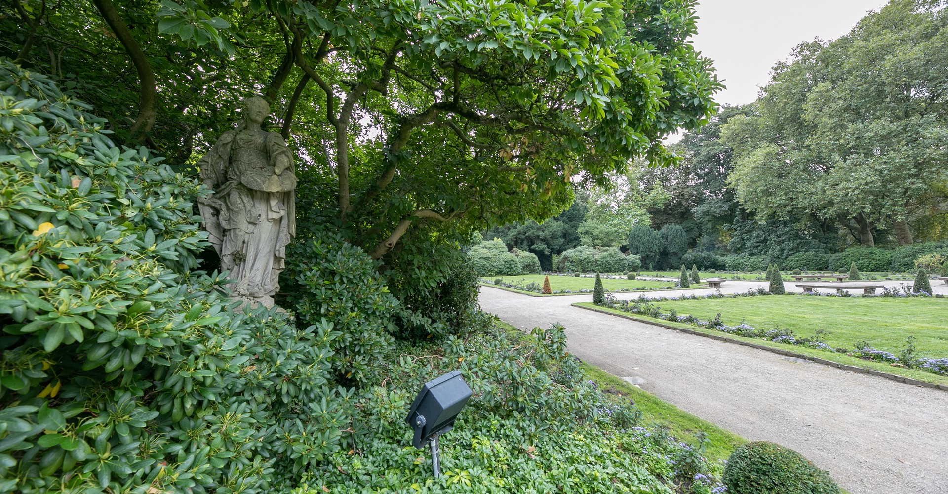 Sandsteinplastiken inmitten dunkellaubiger Rhododendren